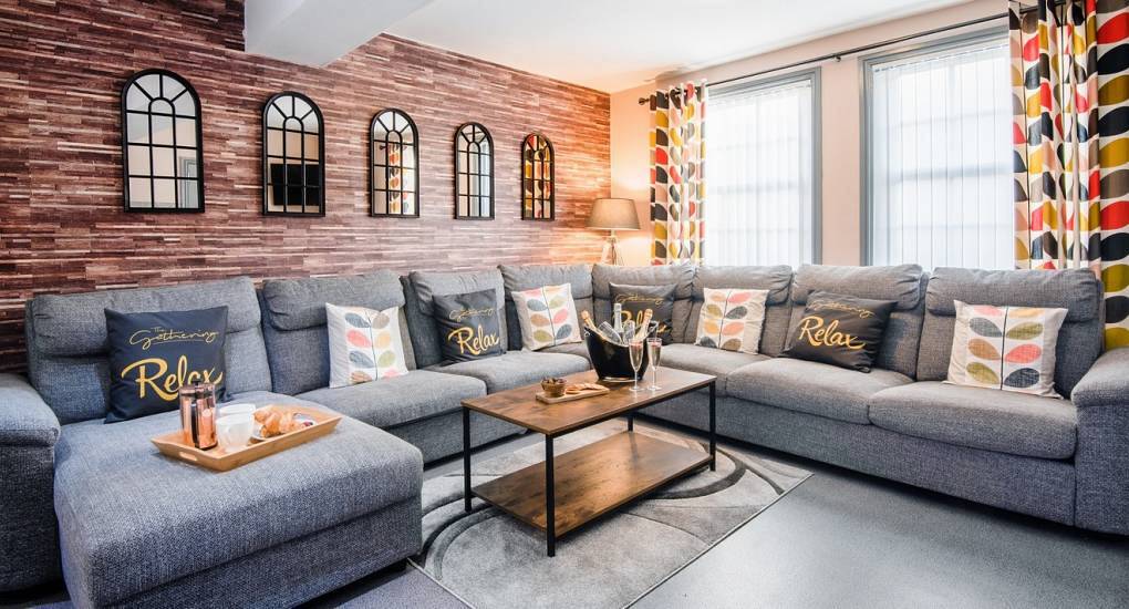 Expansive living room with large grey sectional sofa and brick effect feature wall at The Mews complex in Chester.