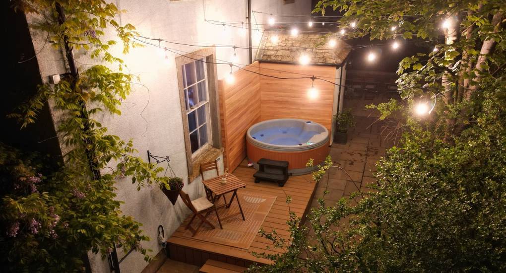 The illuminated patio deck and outdoor hot tub at Hot Tub Charm, a historic Cotswolds hen party house with hot tub.