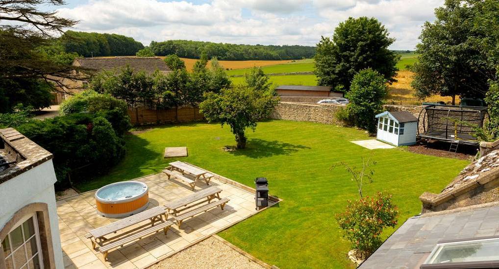 The expansive garden lawn with round hot tub and picnic tables at Cotswolds Oasis, a large hen party house near Bristol.