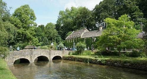 Stone arch bridge over a calm stream with ivy-covered cottages, scenic village backdrop for a Cotswolds stag do.