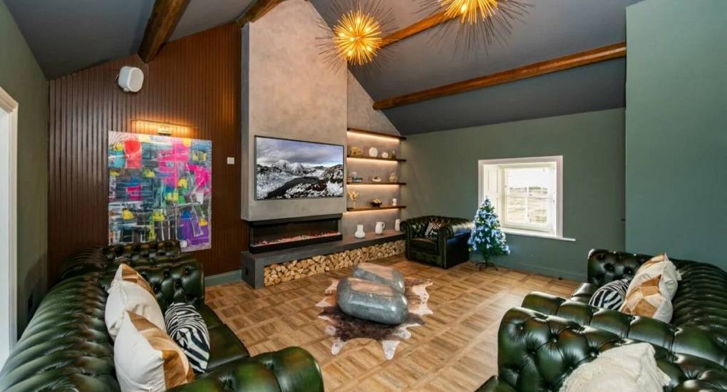 Lounge area with two green Windsor style sofas and large wall mounted tv