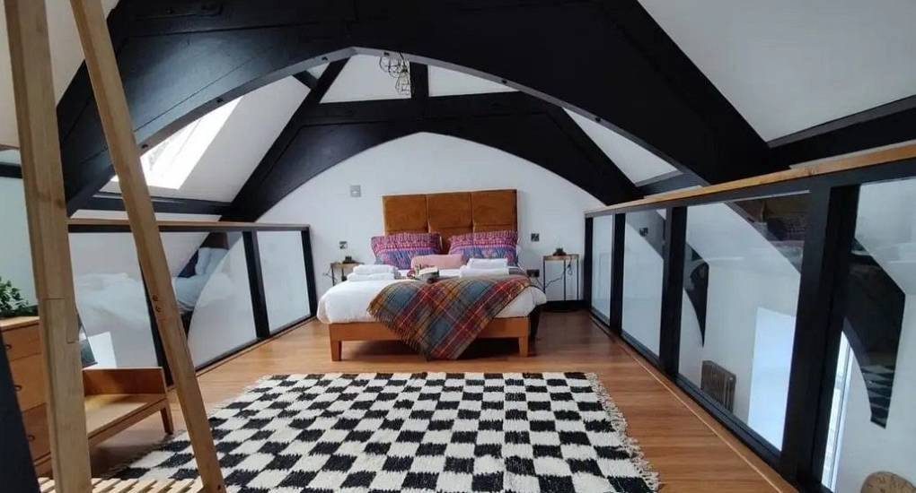 Mezzanine bedroom with checkered rug and dark timber arches at Extravagance, luxury Edinburgh hen apartment.