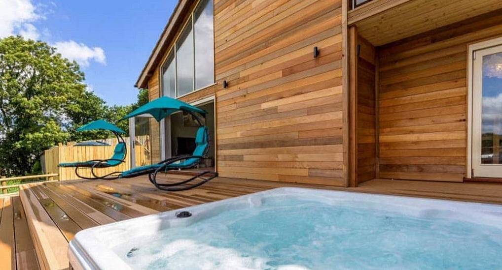 Hot tub on wooden decking with teal swinging sun loungers at The Lake House, secluded Exeter hen party house.