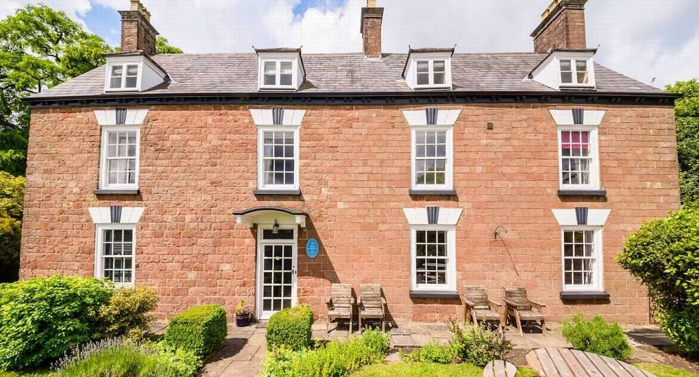 Red sandstone manor house facade with sash windows and garden seating at Deans Forest Retreat in Forest of Dean.