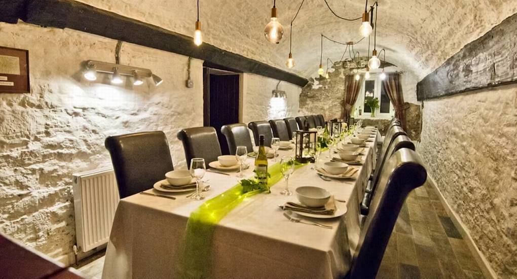 Long banquet dining table under Edison bulb lights in vaulted white stone room at Standing Barn, Gloucestershire.