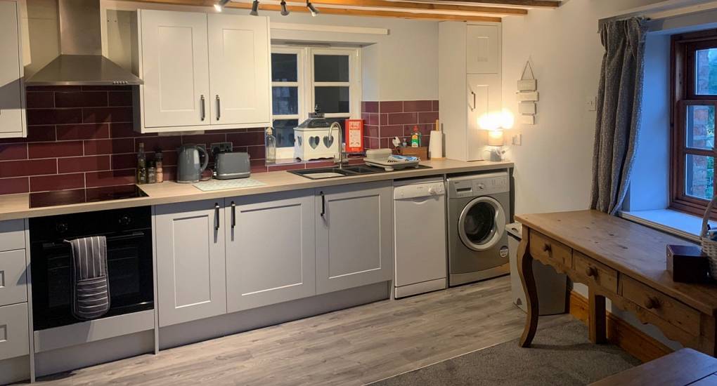 View of the kitchen area with white goods and white cabinets against brick effect wall