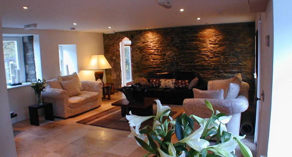 Living room with exposed stone wall, cream sofas and tile flooring at The Jack, luxury party house near Glasgow.