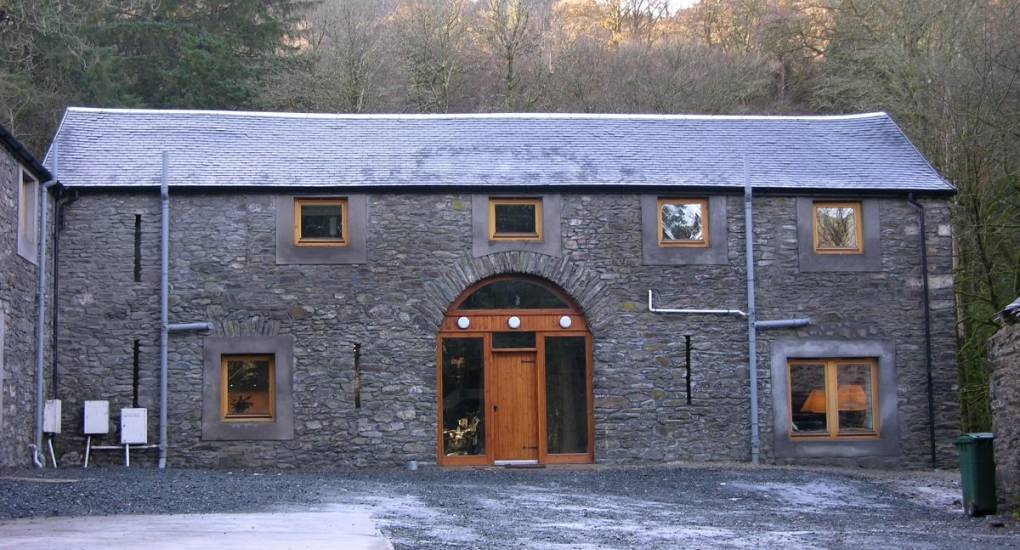 Rustic stone lodge exterior with arched wooden doorway at The Queen, riverside hen party house near Glasgow.