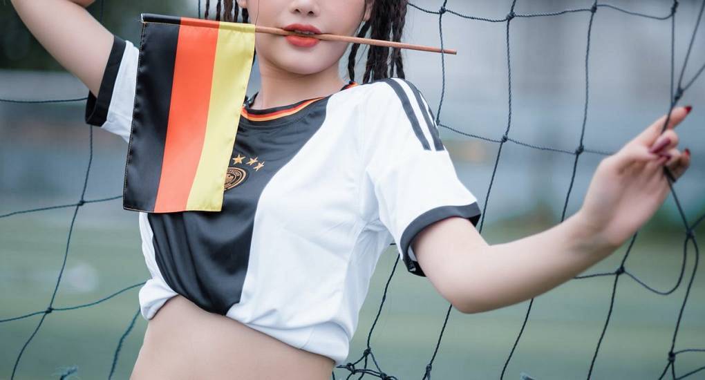 Woman posing in a German football jersey holding a German flag by a goal net, fun setting for a Hamburg stag do.