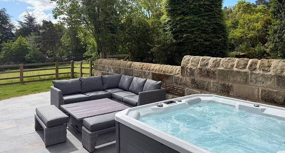 Outdoor paved patio with modern hot tub and grey corner sofa at Hookstone Farmhouse near Harrogate.