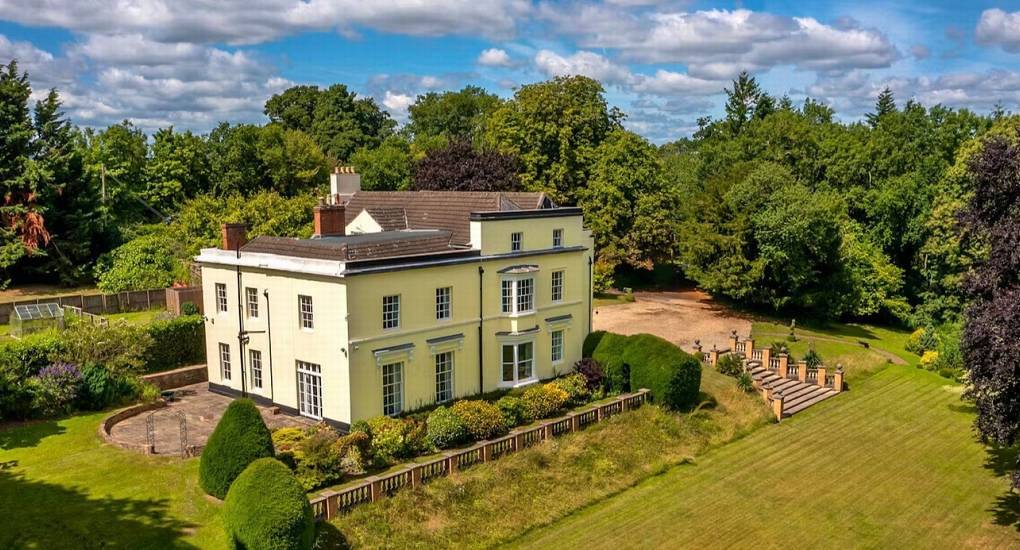 Aerial view of yellow countryside mansion with stone terrace steps and lawns at Rivers Countryside Mansion.