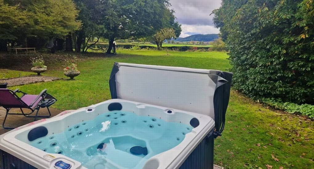Bubbling outdoor hot tub overlooking open green lawns and countryside at The Sash House, Herefordshire.