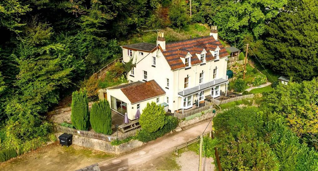 Drone view of three-storey cream house nestled against wooded hillside at Wye House, Herefordshire.