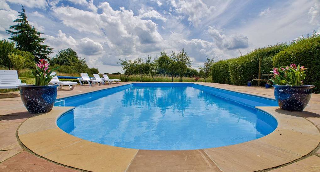 Outdoor swimming pool with sun loungers and potted flowers at Meadowbrook Farm, party house near Ipswich.