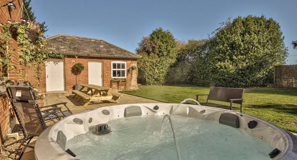 Circular outdoor hot tub with fountain jet on paved patio at River Hall, luxury party house in Ipswich.
