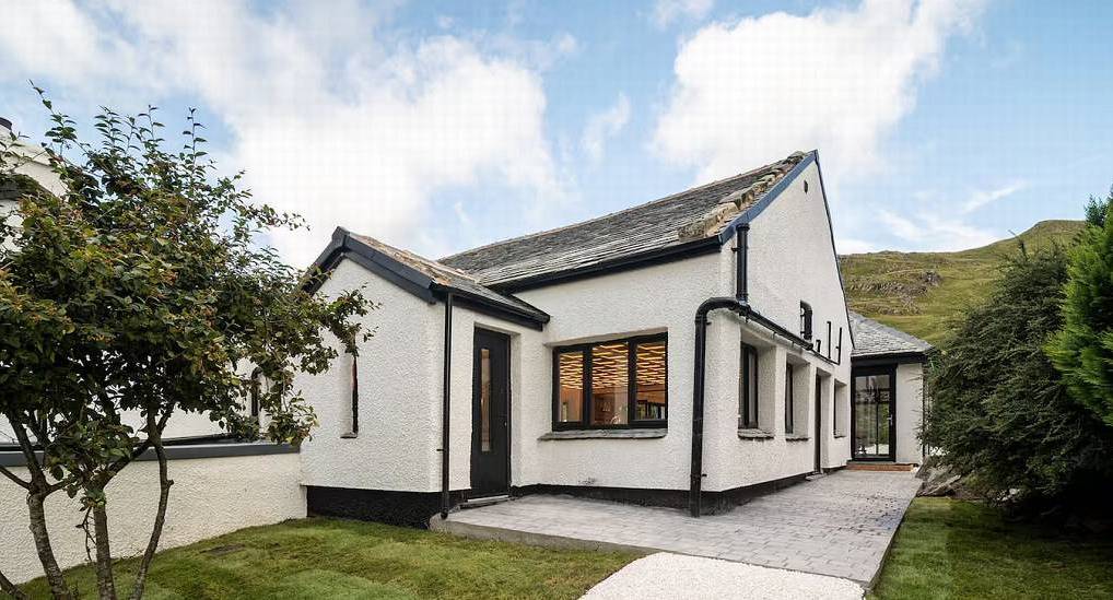 White painted stone cottage with black framed windows and paved patio at King of the Hill in the Lake District.