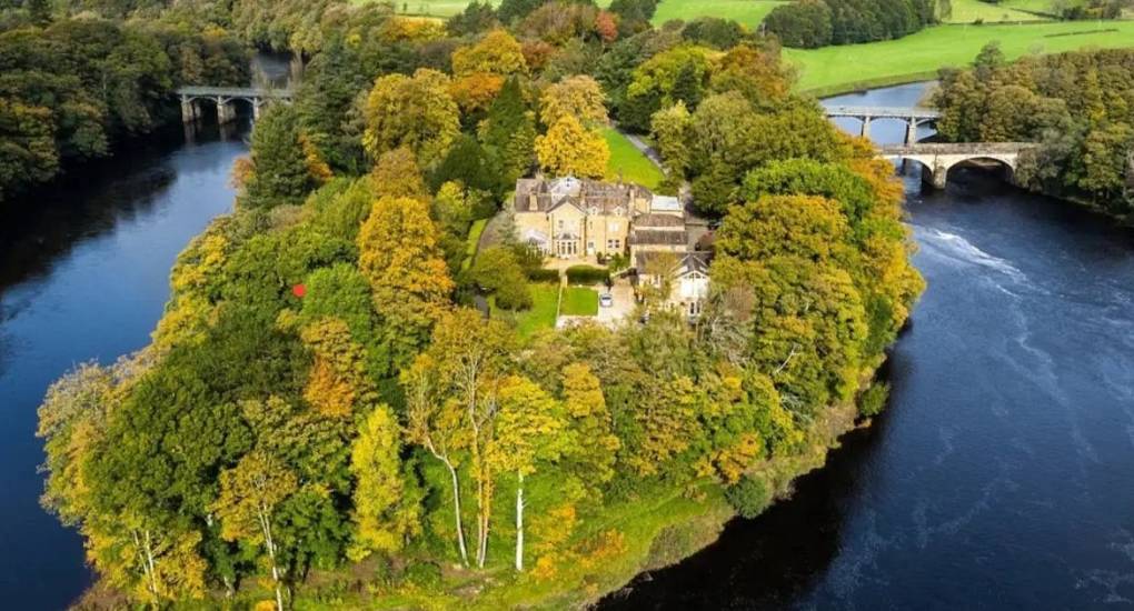 Aerial view of private country estate surrounded by river and autumn woodland at The Island, Lake District.