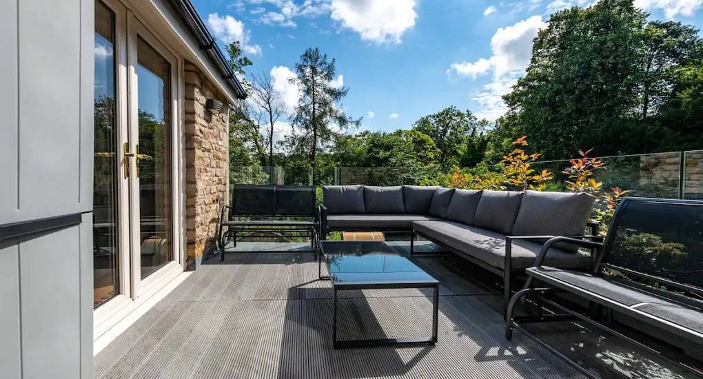 Outdoor decking terrace with sofa seating and glass balcony overlooking green woods at The Rivers, Lake District.