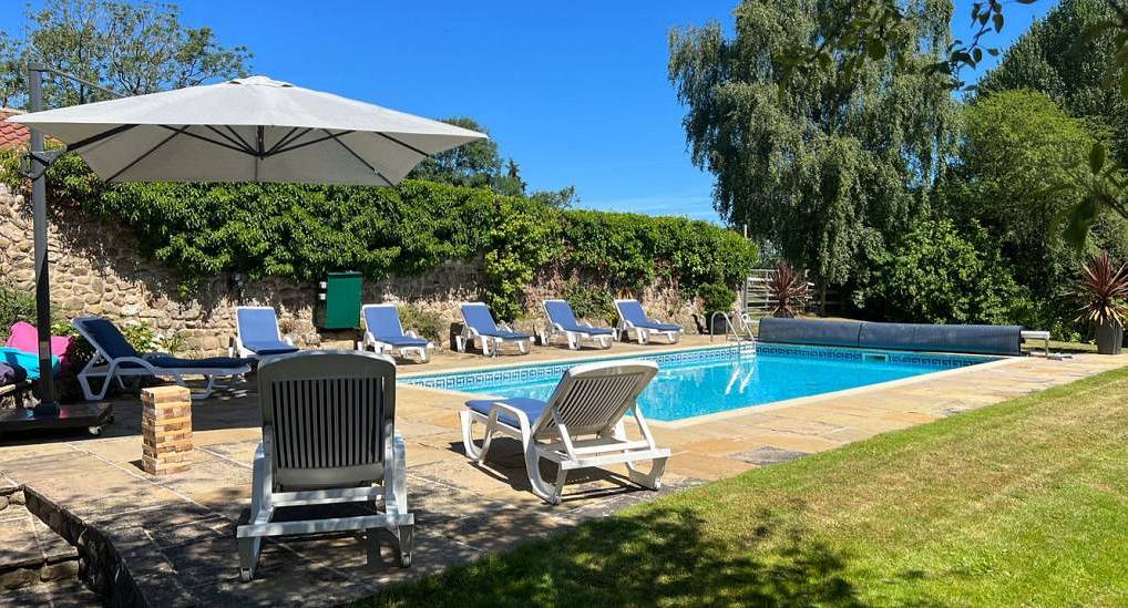 Outdoor swimming pool with sun loungers and parasol on paved terrace at Yorkshire Villa near Leeds and Harrogate.