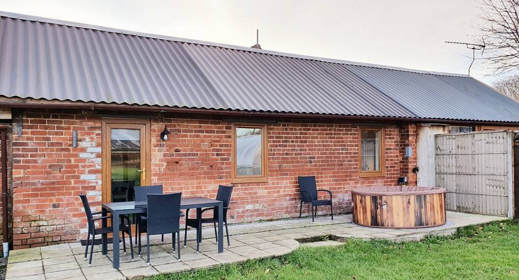 Red brick lodge exterior with patio dining set and circular wooden hot tub at Lincoln Sanctuary lodges.