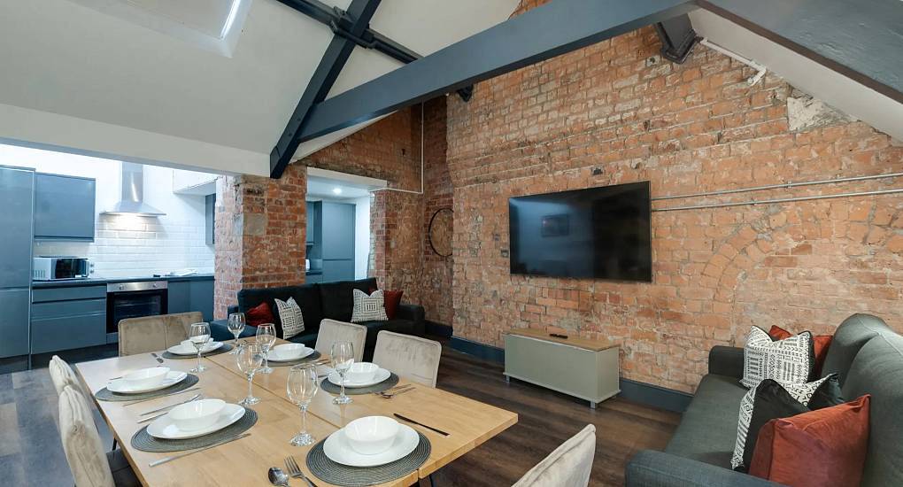 Open plan dining area with wooden table, sofa and exposed brick wall at Harrys apartments in central Liverpool.