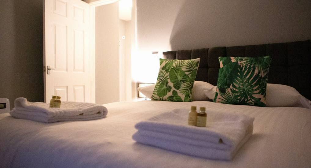 Cosy bedroom with tropical leaf cushions and fresh white towels at The Liver Bird house in Liverpool.