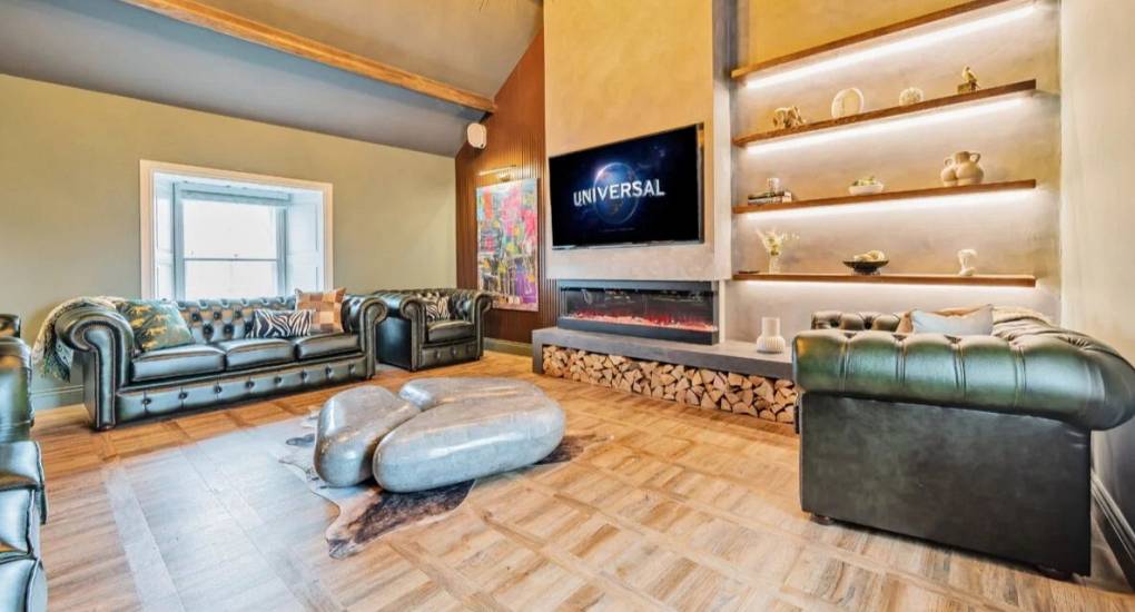 Another view of the lounge area with two sofas and large wall mounted tv and lit shelves with ornaments