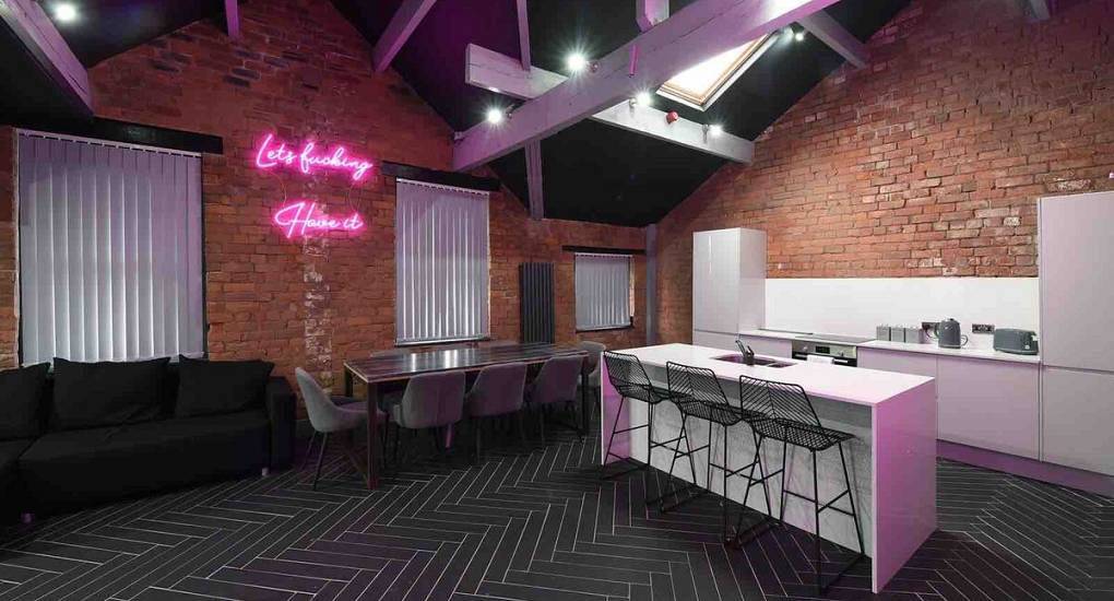 Penthouse lounge with kitchen island, exposed brick wall and neon wall sign at Green Amor 2 in Northern Quarter.