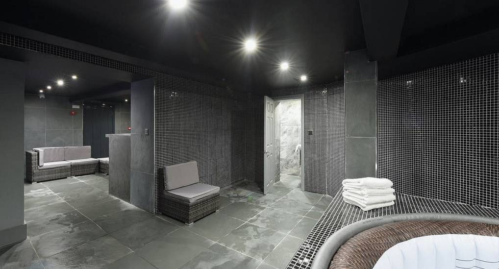 Luxury indoor spa room with black mosaic tiles, lounge seating and hot tub at Green Amor apartments Manchester.
