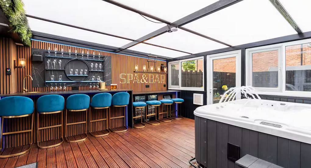 Covered patio spa area with private hot tub, bar counter and blue velvet stools at Irwell Villa Manchester.