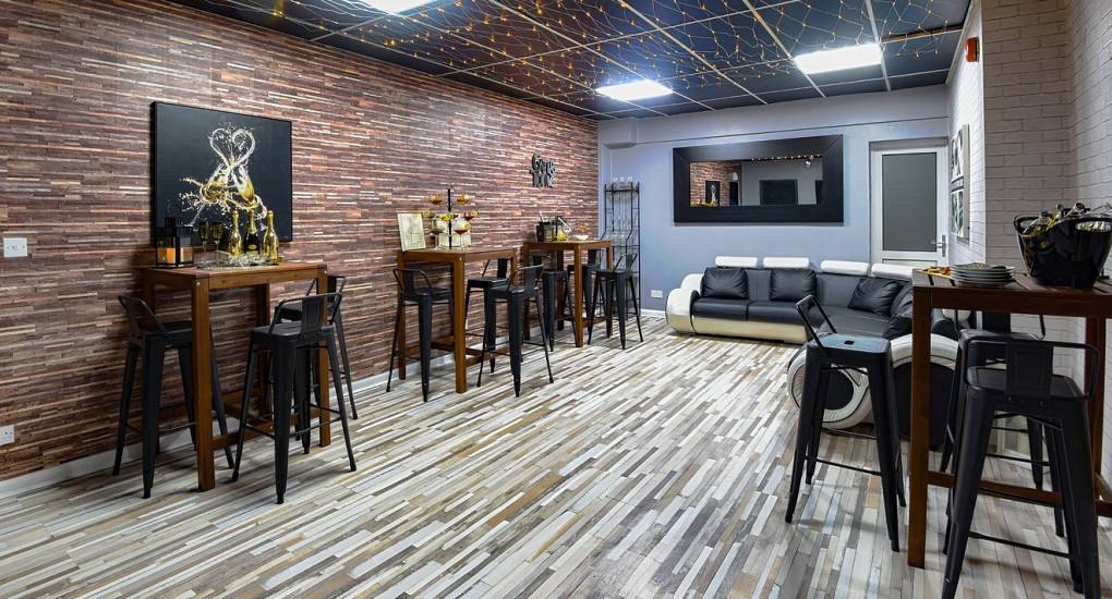 Private bar area with wood panel wall, high tables, black stools and leather sofa at The Docks near Manchester.