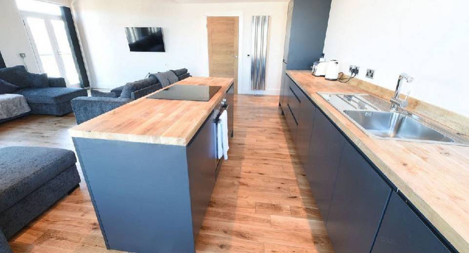 Modern kitchen island with wood countertop and grey sofa area at The Reds 20 apartments near Northern Quarter.