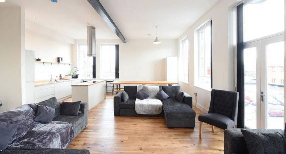 Expansive living room with grey corner sofas and large windows at The Reds group apartments in Manchester.