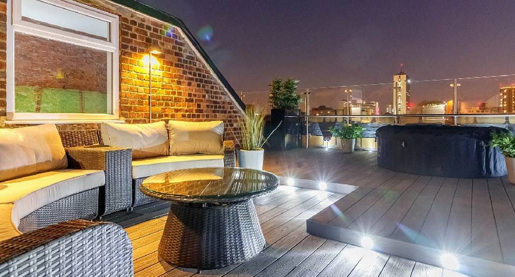 Rooftop terrace with outdoor wicker sofas and hot tub overlooking city lights at The White House Manchester.