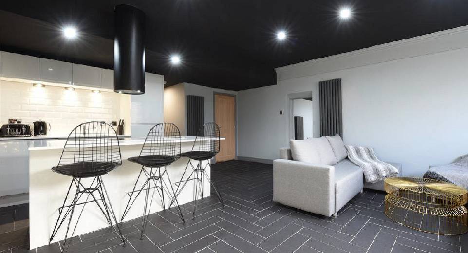 Modern white kitchen island with black wire bar stools and grey sofa at The White Suite in Northern Quarter Manchester.