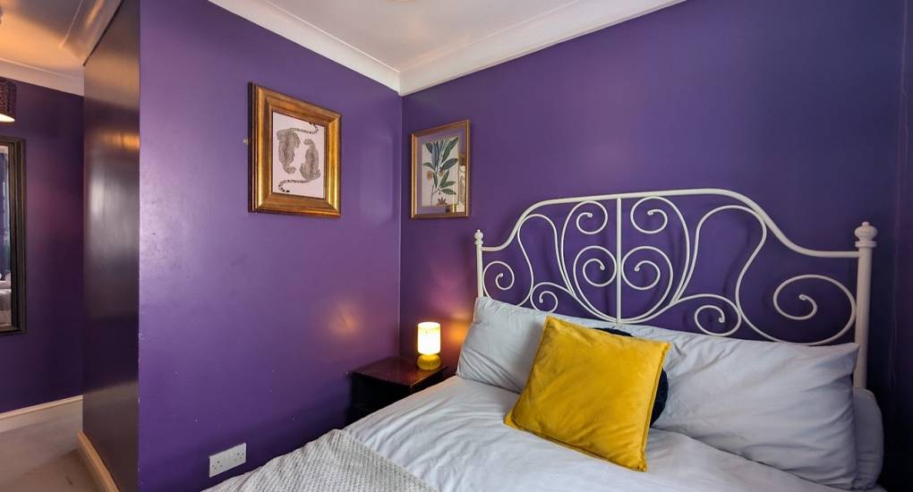 Master bedroom with royal purple walls and a made up double bed
