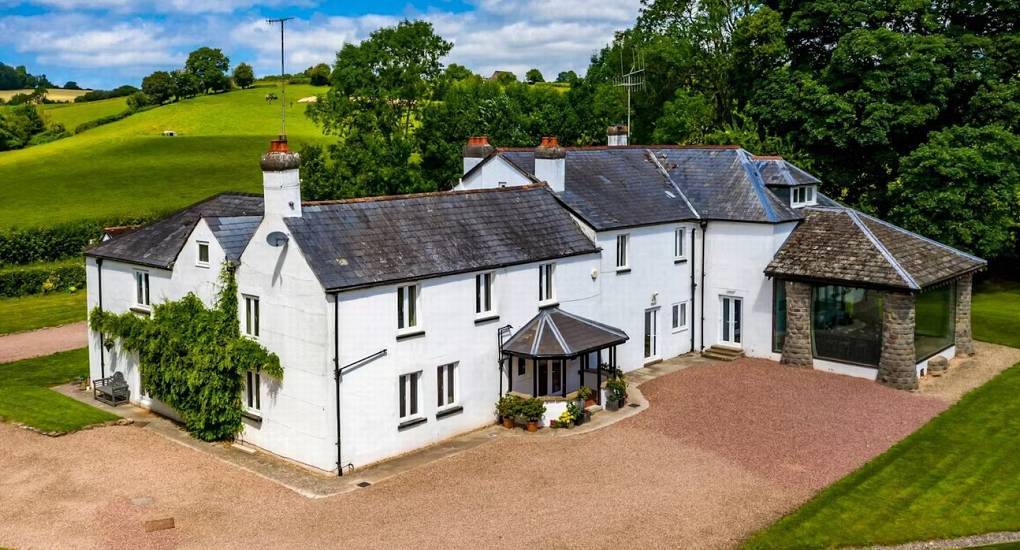 White countryside mansion house with gravel driveway and lush green hills view at Musician's Manor Monmouthshire.