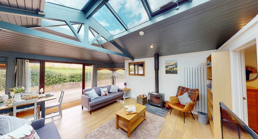 Bright modern living area with ceiling skylight, log burner stove, cozy sofas and dining table at New Forest Manor.