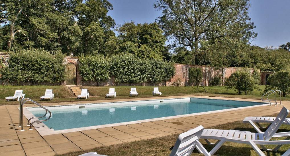 Large outdoor swimming pool with white lounge chairs, paved terrace and walled garden at Riverstone near Salisbury.