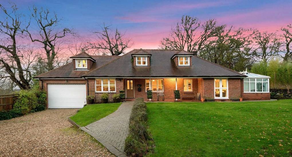 Wide brick country house exterior with dormer windows, conservatory and green lawn at dusk at The Paddocks New Forest.
