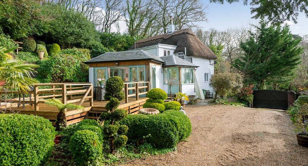 Traditional thatched cottage with wooden decking terrace, garden conservatory and gravel driveway in New Forest.