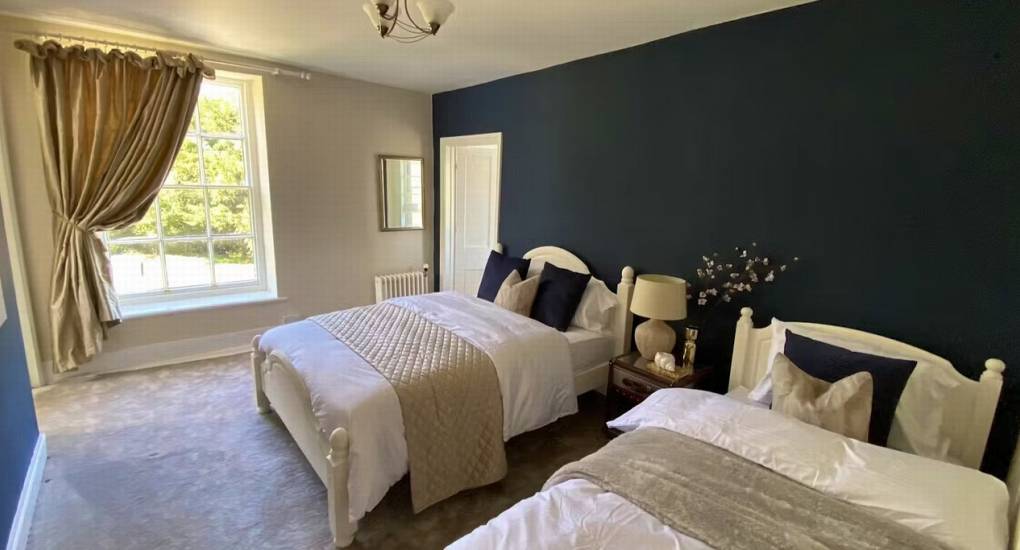 A comfortable bedroom at the Wye Valley hen party house with two twin beds and stylish navy blue feature wall.