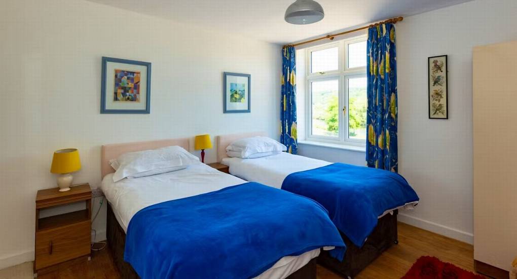 A bright twin bedroom at Ross Lodge Gloucestershire with vibrant blue bedspreads, part of the extensive hen do accommodation that sleeps 26.