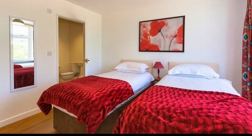 A comfortable twin bedroom at Ross Lodge Gloucestershire featuring striking red bedspreads and an en-suite bathroom, ideal for a Gloucestershire hen do accommodation stay.