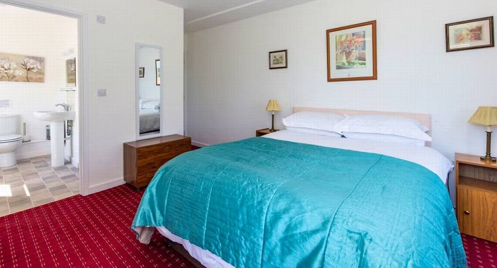 A double bedroom at Ross Lodge Gloucestershire with a teal bedspread and an en-suite, one of the many rooms at this spacious hen do accommodation.