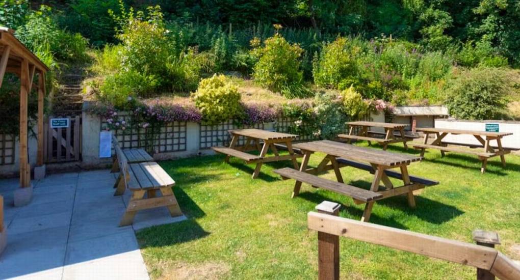 The large garden area at Ross Lodge Gloucestershire featuring wooden picnic tables and benches, perfect for outdoor dining at this hen do accommodation that sleeps 26.