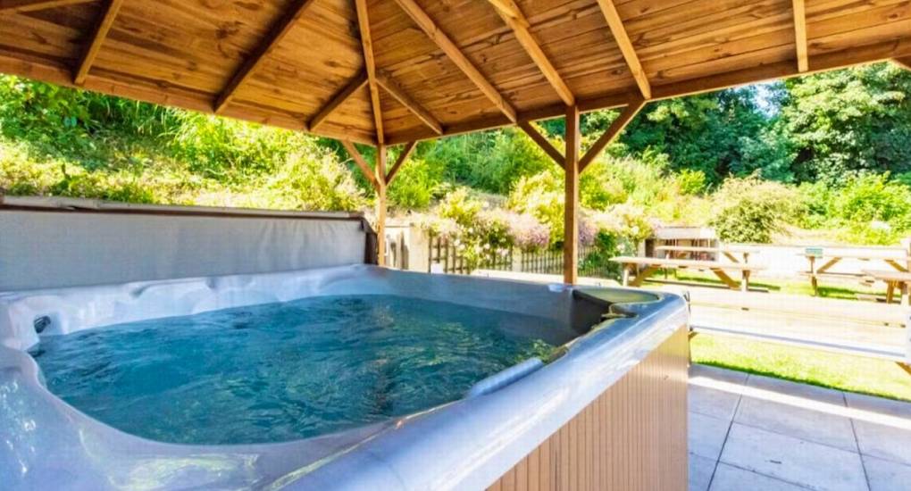 The large, bubbling hot tub at Ross Lodge Gloucestershire under a wooden gazebo, providing a relaxing luxury feature for this hen do accommodation.