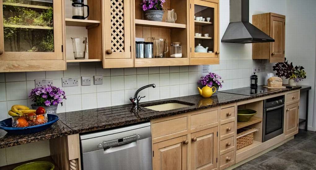 The main self-catering kitchen at Ross Lodge Gloucestershire featuring natural wood cabinets and granite countertops, providing plenty of space for a hen do group that sleeps 26.