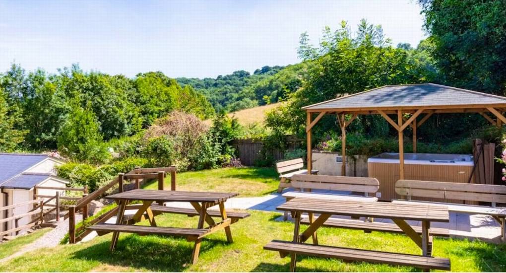 The covered hot tub at Ross Lodge Gloucestershire, situated near wooden picnic benches and overlooking the Gloucestershire countryside.
