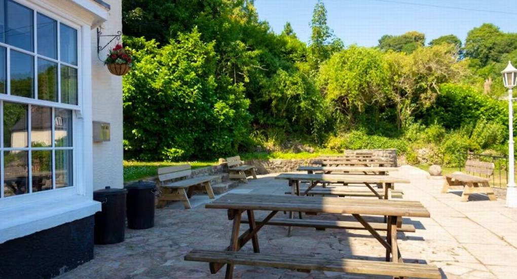 The sunny patio area at Ross Lodge Gloucestershire featuring multiple wooden picnic tables, providing outdoor seating for the large hen do group that sleeps 26.